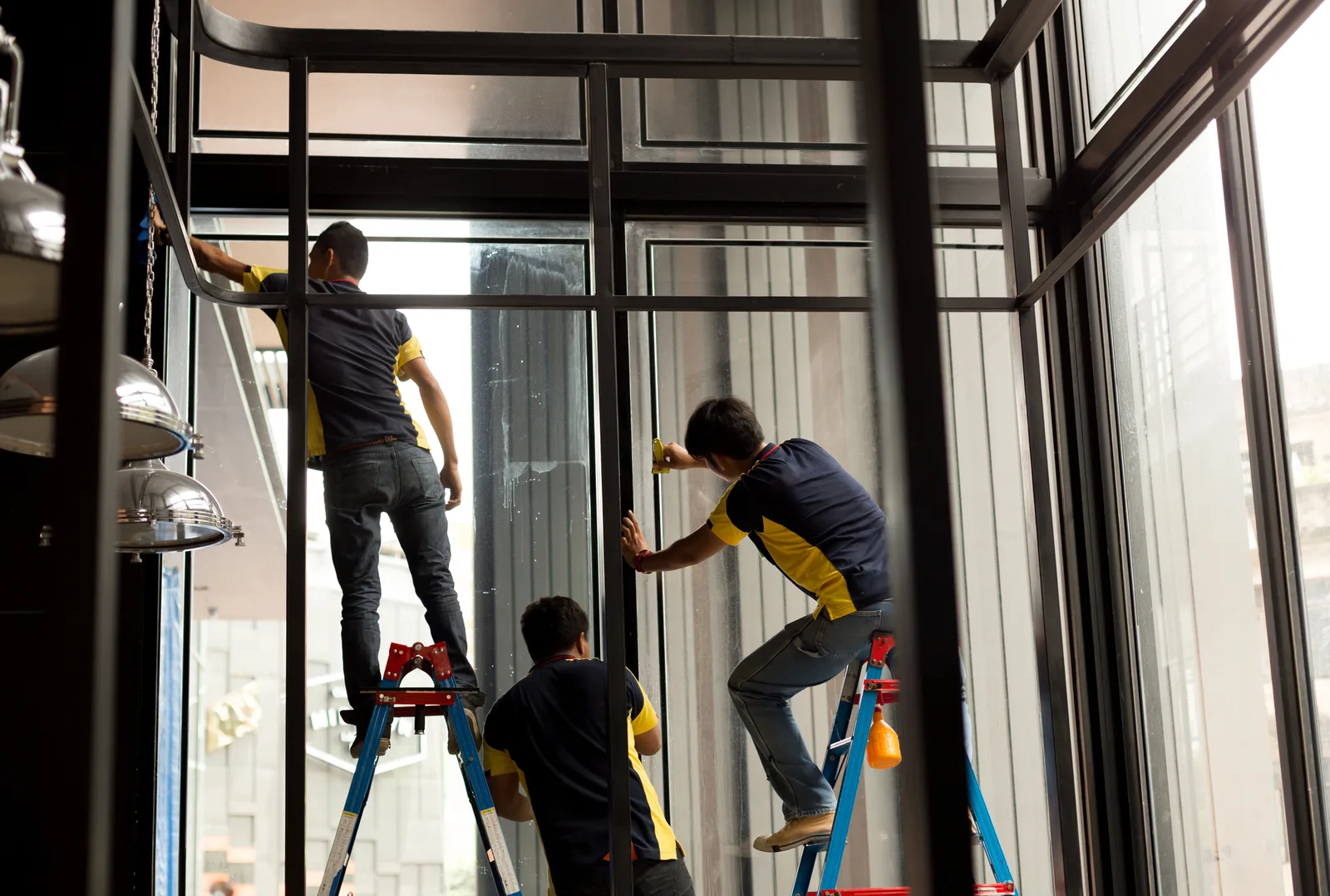 A crew on ladders applying window film across tall commercial glass panels.